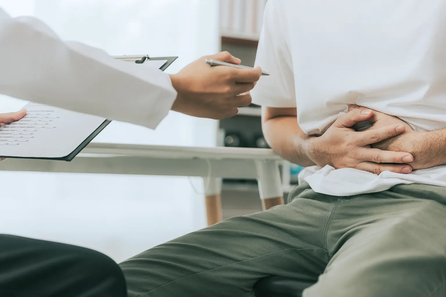 Doctor counseling male patient with abdominal pain in hospital examination room
